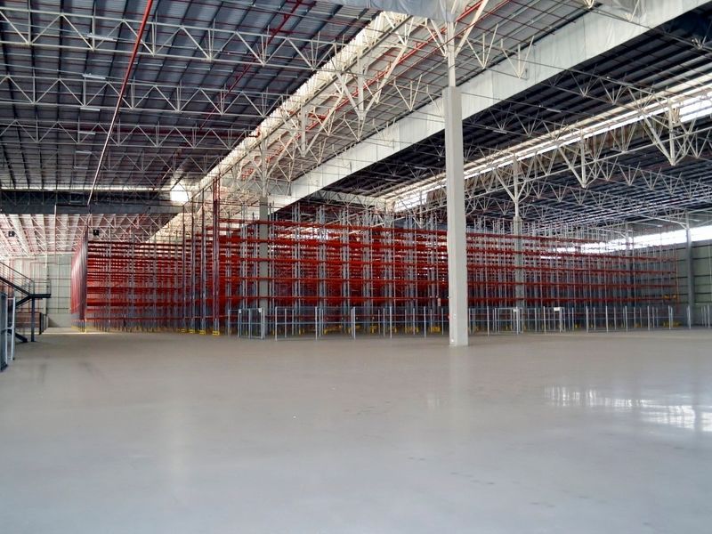 Spacious industrial warehouse featuring high ceilings with exposed steel trusses, polished concrete flooring, and extensive built-in steel racking systems.