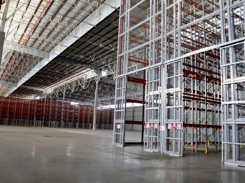 Spacious industrial warehouse featuring high-clearance steel roof trusses, polished concrete flooring, and extensive built-in heavy-duty steel racking systems.
