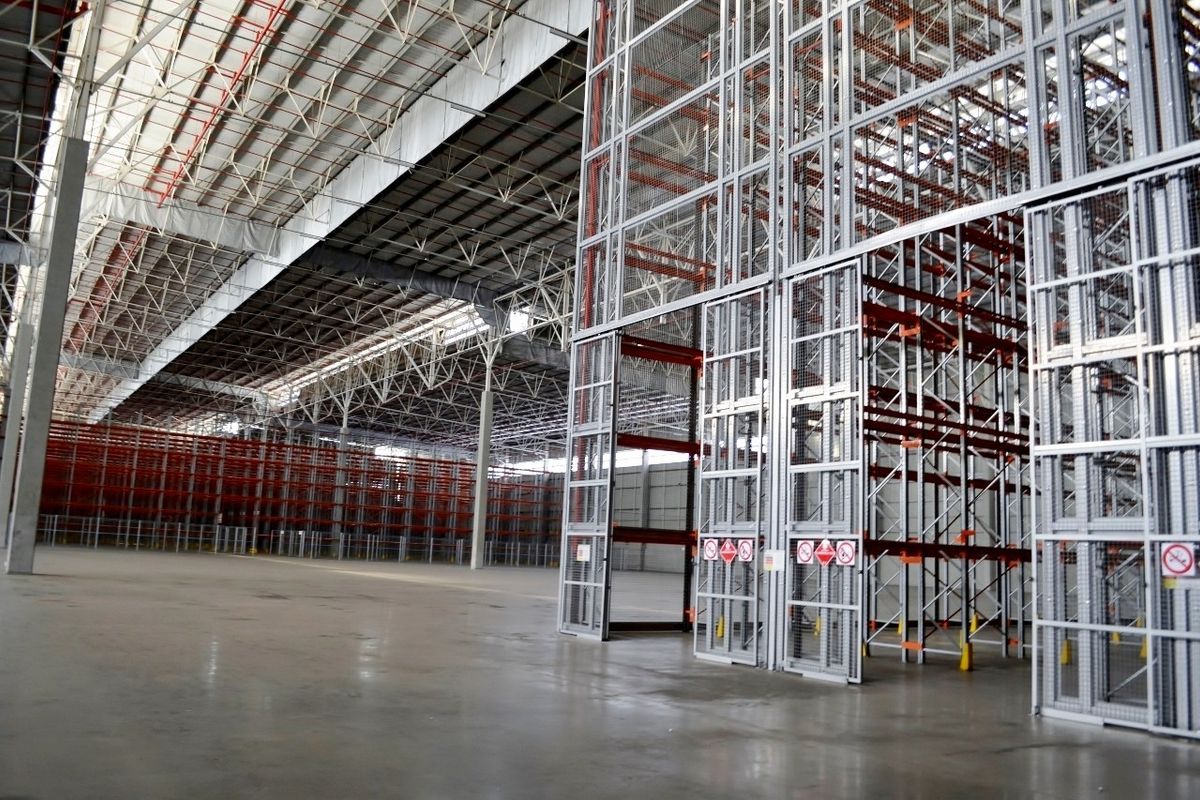 Spacious industrial warehouse featuring high-clearance steel roof trusses, polished concrete flooring, and extensive built-in heavy-duty steel racking systems.