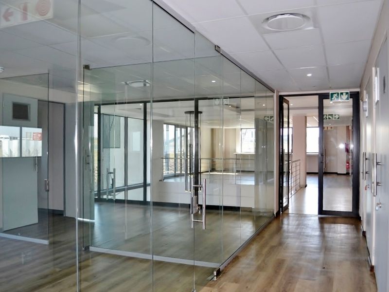 Modern office space featuring glass partitioning, suspended ceilings with recessed lighting, and durable laminate flooring in a clean, professional industrial setting.