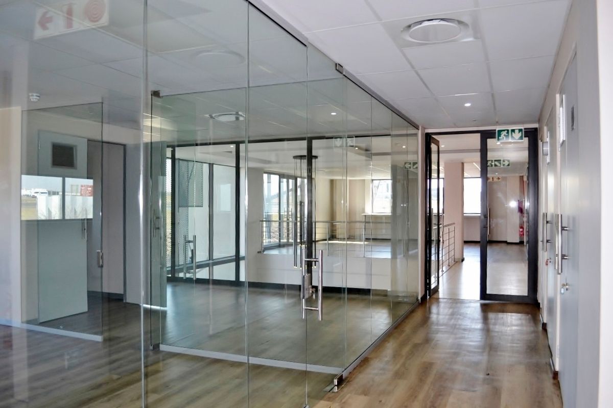 Modern office space featuring glass partitioning, suspended ceilings with recessed lighting, and durable laminate flooring in a clean, professional industrial setting.