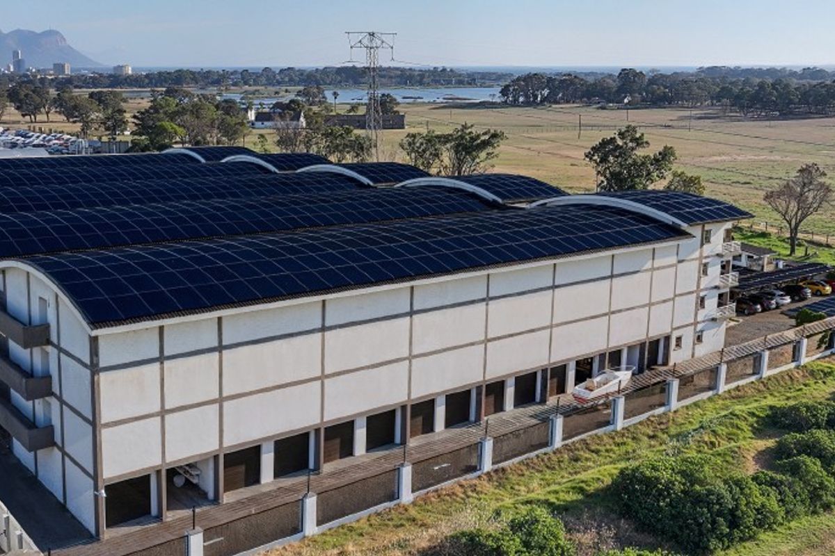 Aerial view of a large commercial warehouse facility featuring an extensive rooftop solar panel installation and secure perimeter fencing.