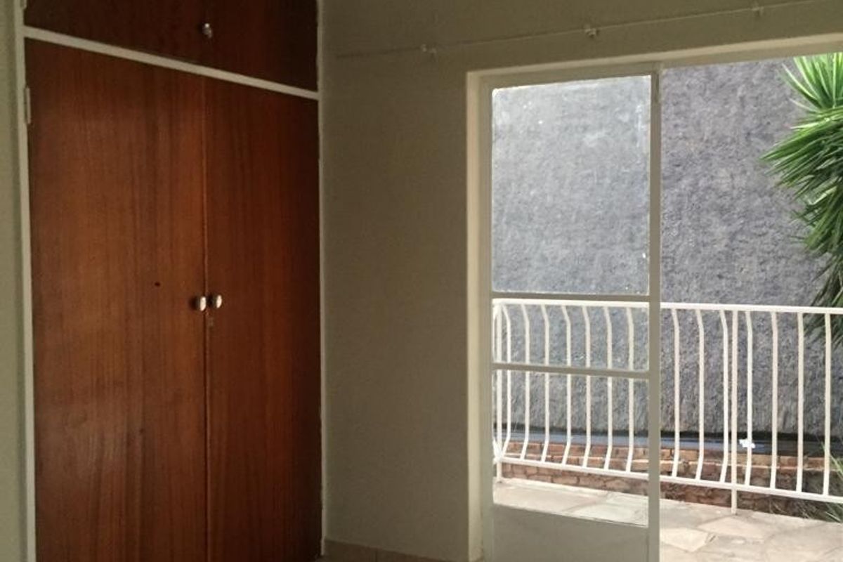 An empty bedroom featuring built-in wooden cupboards, tiled flooring, and a sliding glass door providing access to a small balcony area.