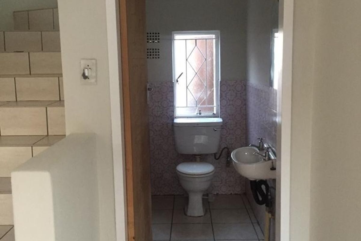 A compact guest bathroom featuring ceramic floor tiles, a wall-mounted basin, and a standard flush toilet, located adjacent to the staircase.