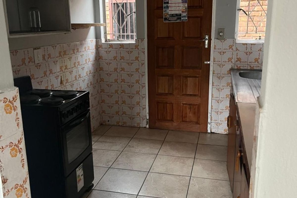 A functional kitchen featuring tiled flooring, built-in cabinetry, a sink, and a freestanding stove, with dated finishes ready for modernization.