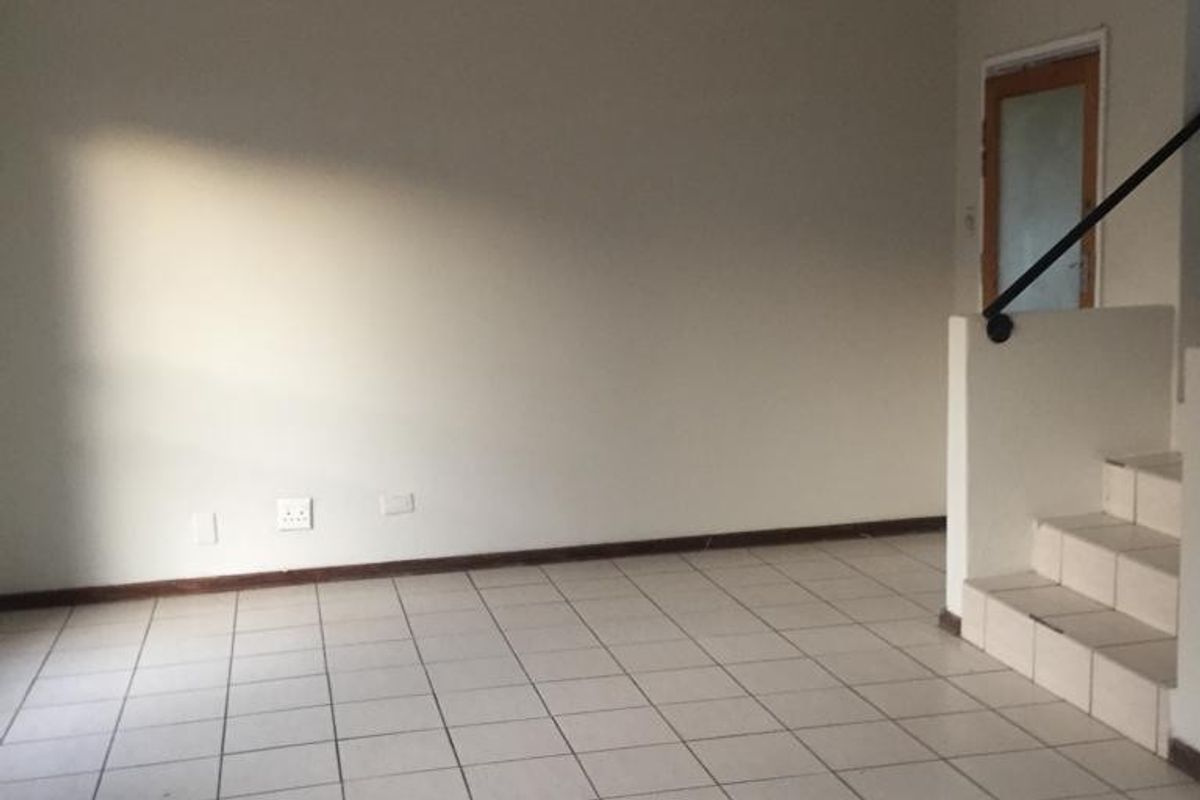 An empty living area featuring neutral tiled flooring, a staircase with a handrail, and plain walls, offering a blank canvas for interior design.