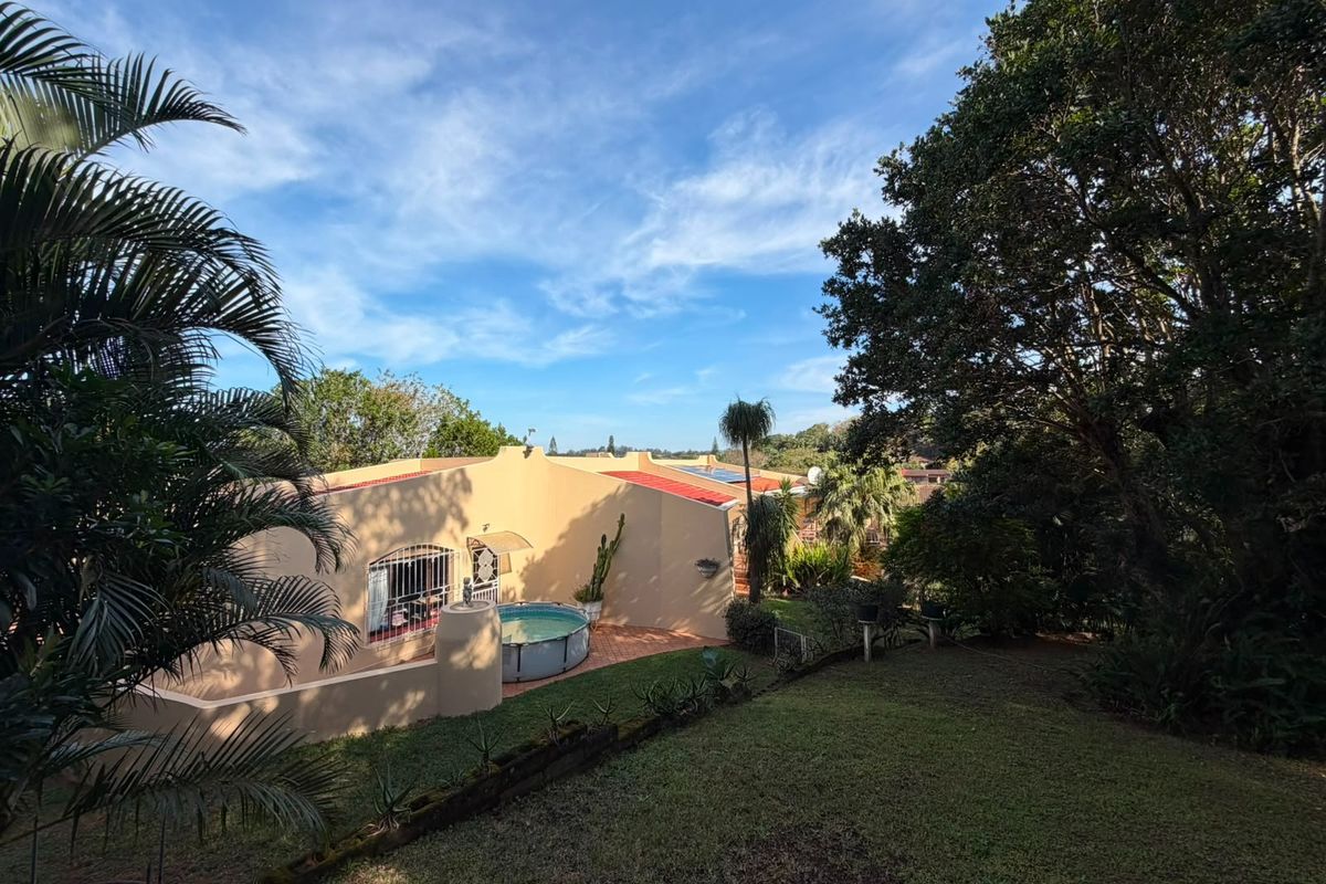Rear view of the property featuring a swimming pool, landscaped garden, and solar panels installed on the tiled roof.