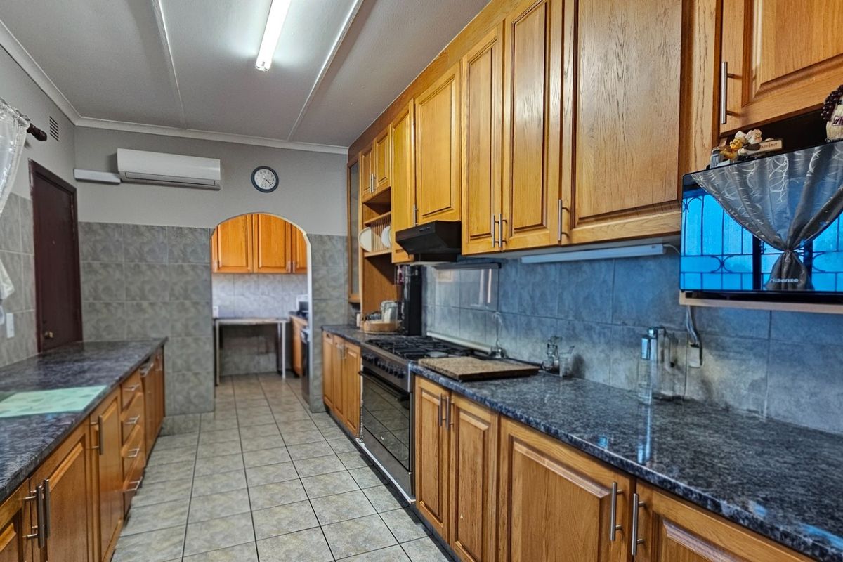 A functional kitchen featuring wooden cabinetry, granite countertops, a gas hob with extractor fan, and tiled finishes, with an adjoining scullery area.