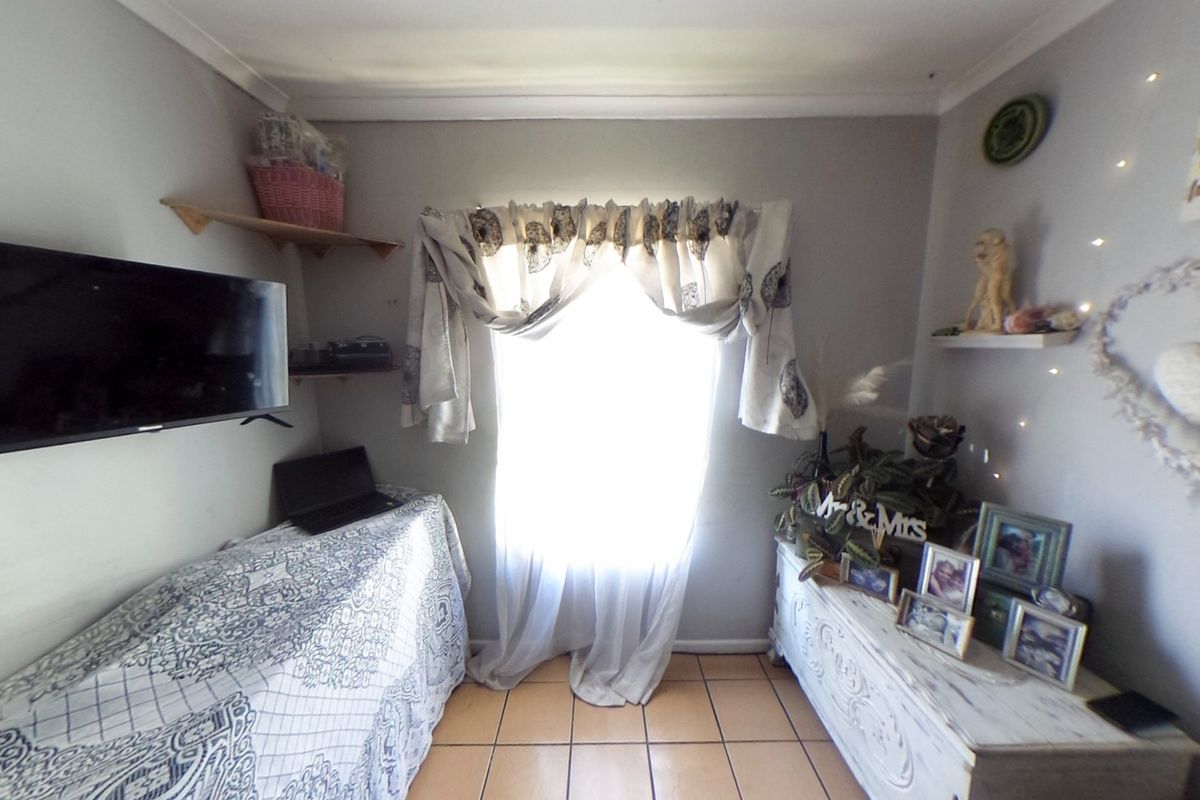A compact bedroom featuring tiled flooring and a wall-mounted security alarm keypad, offering a functional space with neutral wall finishes.