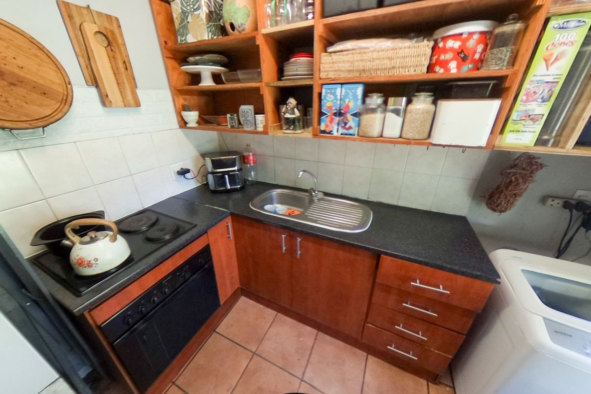 Compact kitchen featuring wooden cabinetry, built-in oven, electric hob, stainless steel sink, and tiled backsplash with practical open shelving for storage.