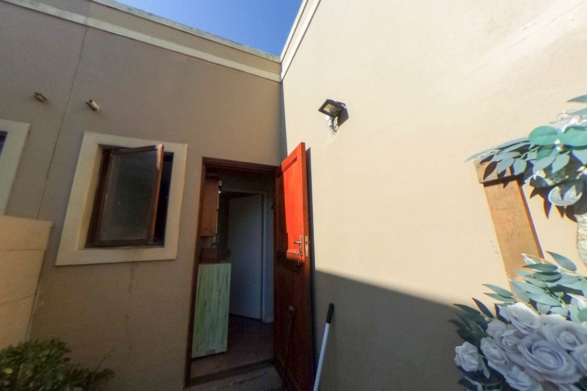 A view of the rear exterior wall featuring a timber door, a casement window, and an external wall-mounted light fixture.