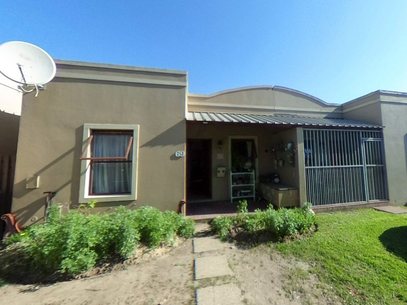 Front elevation of a townhouse featuring a covered entrance, security gate, satellite dish, and a small garden area with a paved walkway.