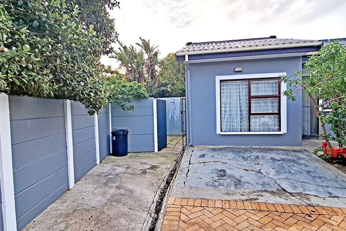 Rear exterior view of the apartment featuring a concrete paved area, precast boundary wall, and tiled roof structure.