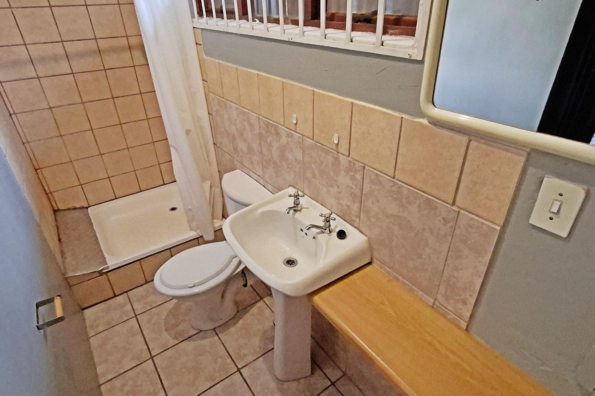 A compact bathroom featuring a pedestal basin, toilet, and shower tray with tiled finishes and security bars on the window.