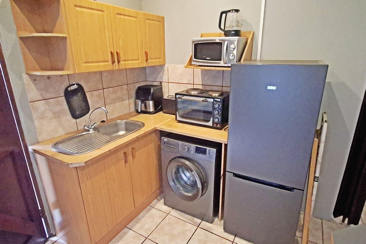 Compact kitchen featuring light wood-look cabinetry, tiled backsplash, stainless steel sink, and integrated space for a washing machine.