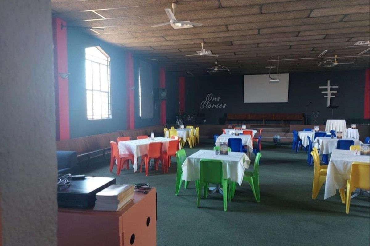 Large open-plan commercial hall featuring a raised stage, projector screen, built-in bench seating, and ceiling fans, suitable for events or community gatherings.