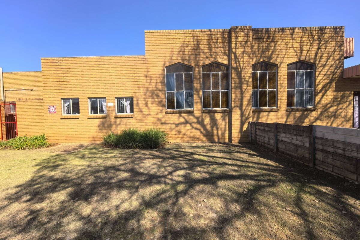 Rear exterior view of a commercial brick building featuring multiple windows with security bars and a precast concrete boundary wall.