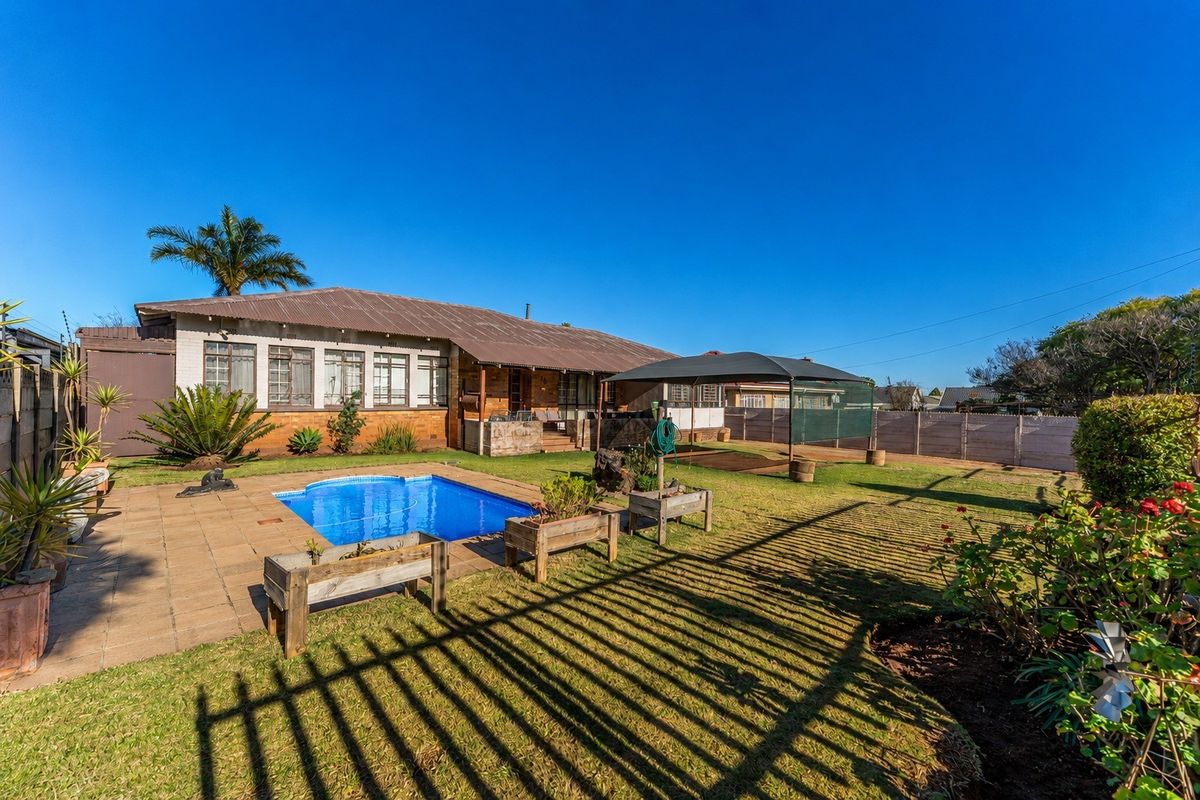 Rear view of the property featuring a swimming pool, paved patio area, and a spacious garden with perimeter fencing.