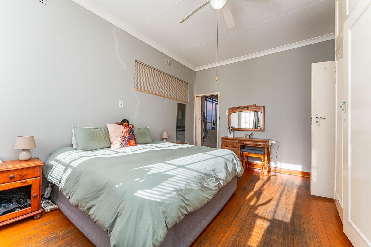 A bedroom featuring timber flooring, a ceiling fan, and built-in wardrobe storage, with visible wall plaster cracks and dated finishes.
