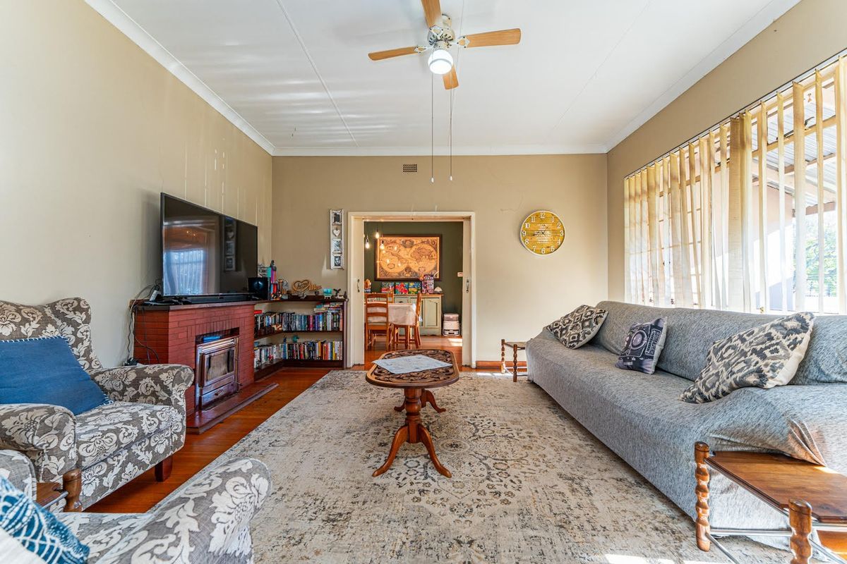 Spacious living room featuring a brick fireplace, built-in shelving, hardwood flooring, and a ceiling fan, offering a comfortable and functional living space.
