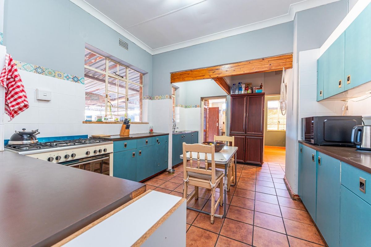A functional kitchen featuring blue cabinetry, tiled flooring, a gas stove, and an exposed timber beam, offering a classic layout with potential for modernization.