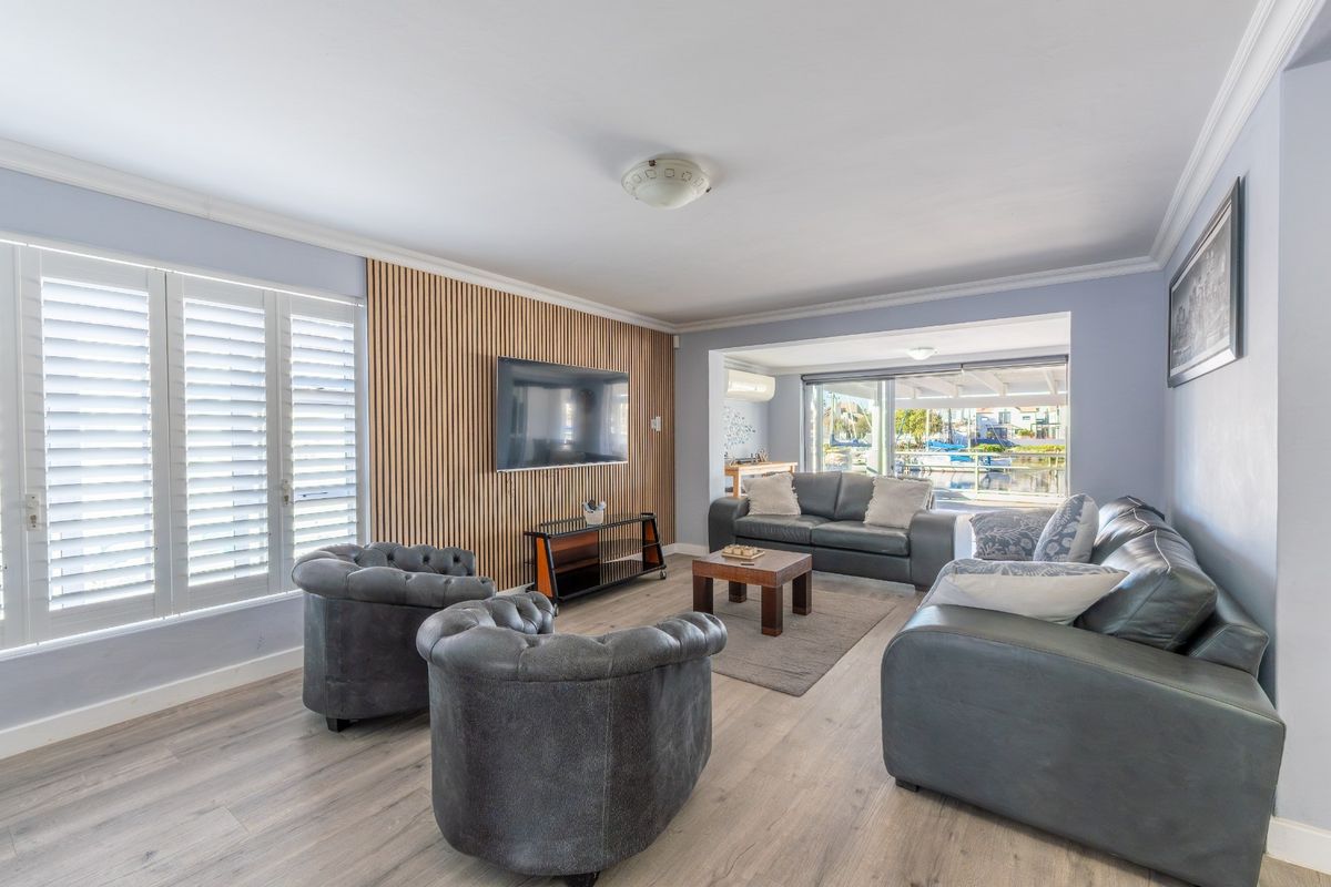 Spacious living room featuring a modern timber slat feature wall, plantation shutters, and light-toned laminate flooring with direct access to the outdoor area.