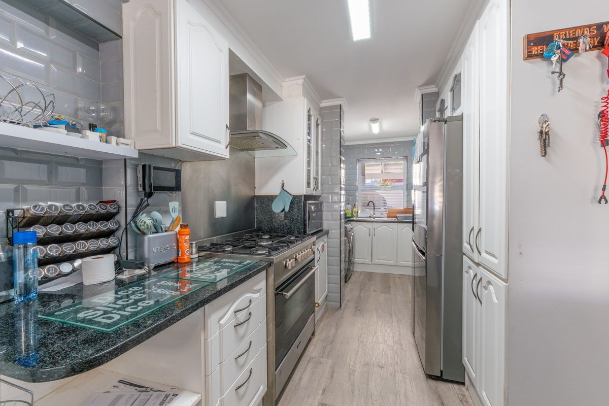 A functional galley-style kitchen featuring white cabinetry, granite countertops, subway tile backsplash, and a gas hob with an integrated extractor fan.
