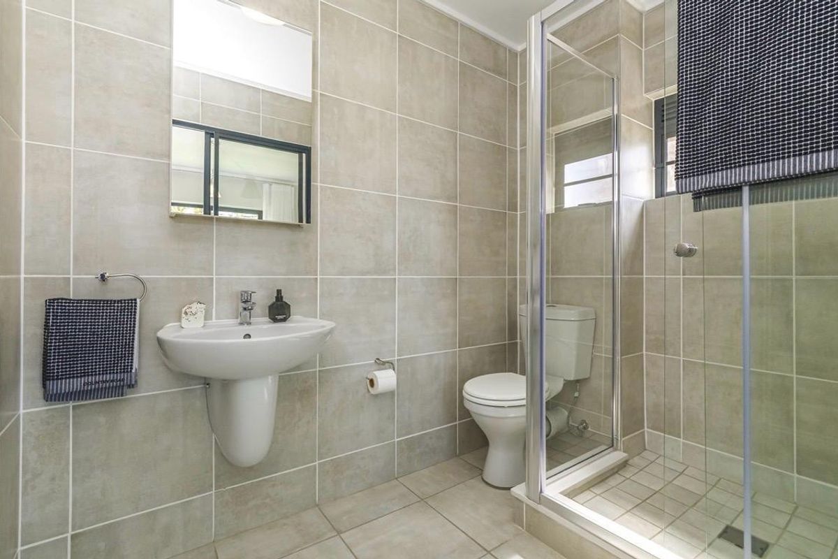 A clean, modern bathroom featuring neutral wall and floor tiles, a pedestal washbasin, and a glass-enclosed shower unit.