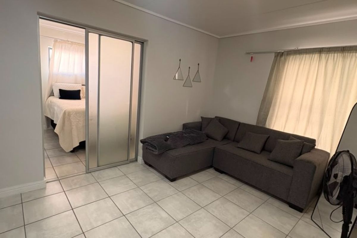A living room featuring neutral tiled flooring and a sliding glass door providing access to an adjacent bedroom.