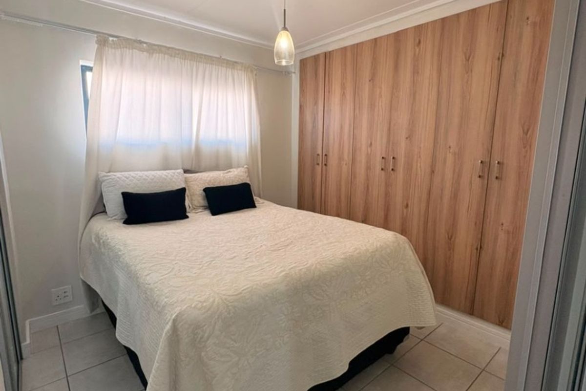 A well-maintained bedroom featuring neutral tiled flooring, a coved ceiling, and extensive floor-to-ceiling built-in wooden cupboards for ample storage.