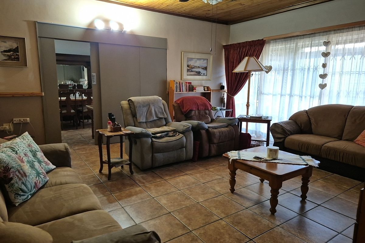 A comfortable living room featuring tiled flooring, a timber-paneled ceiling with a ceiling fan, and a sliding door leading to an adjacent dining area.