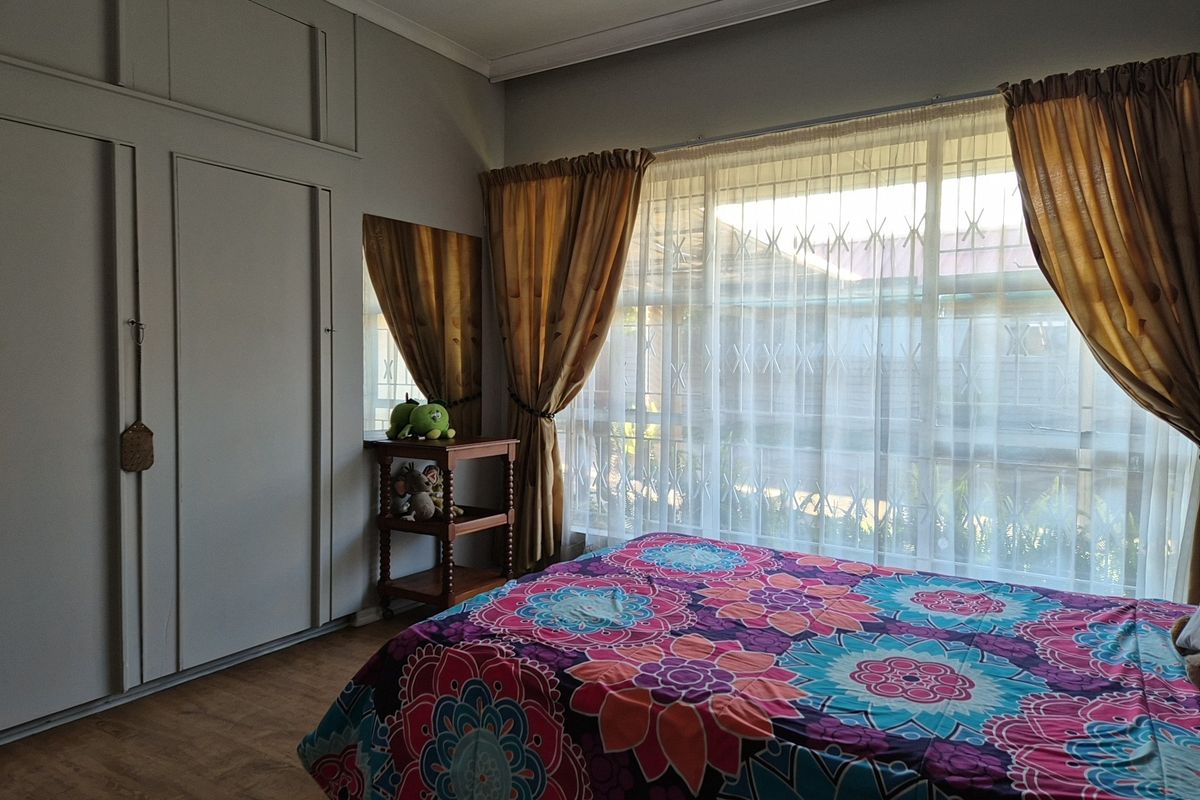 A bedroom featuring built-in cupboards, laminate flooring, and a large window fitted with a security gate.
