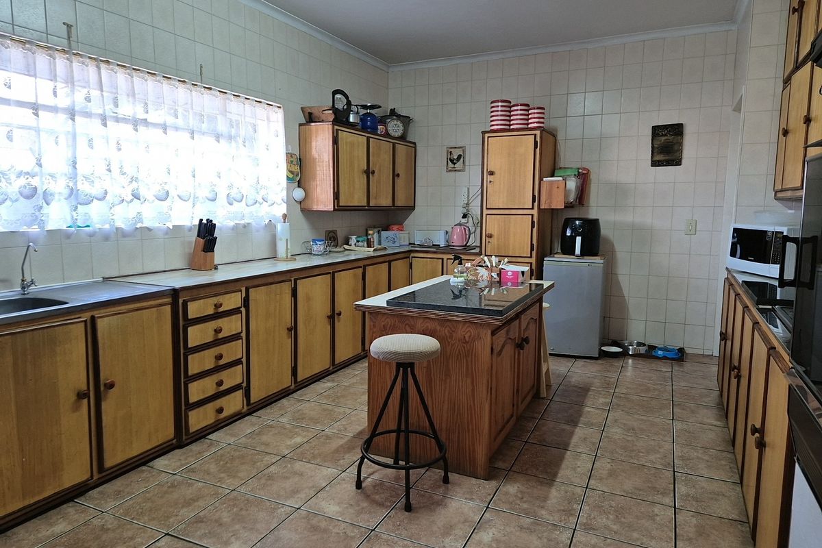 A spacious kitchen featuring traditional wooden cabinetry, a central island with a stone countertop, tiled walls, and durable floor tiles.