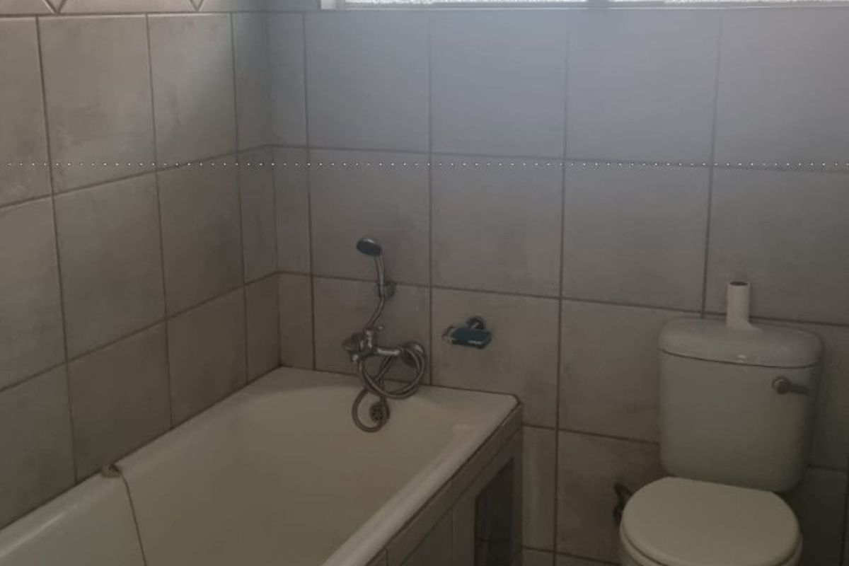 A functional bathroom featuring a bathtub, toilet, and tiled finishes, requiring cosmetic updates to improve its overall condition and aesthetic appeal.
