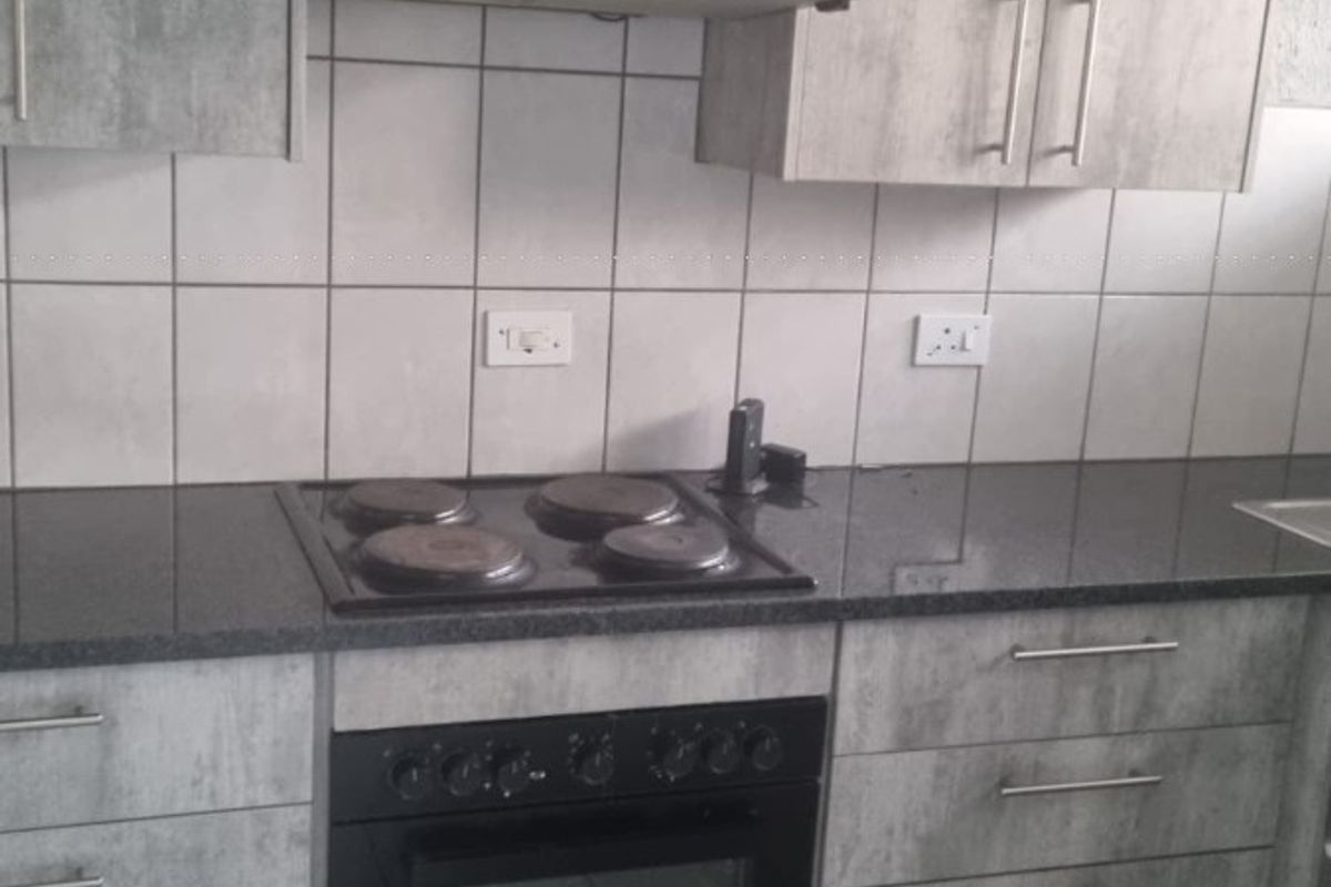 A functional kitchen featuring grey textured cabinetry, granite countertops, a built-in oven, electric hob, and a tiled backsplash.