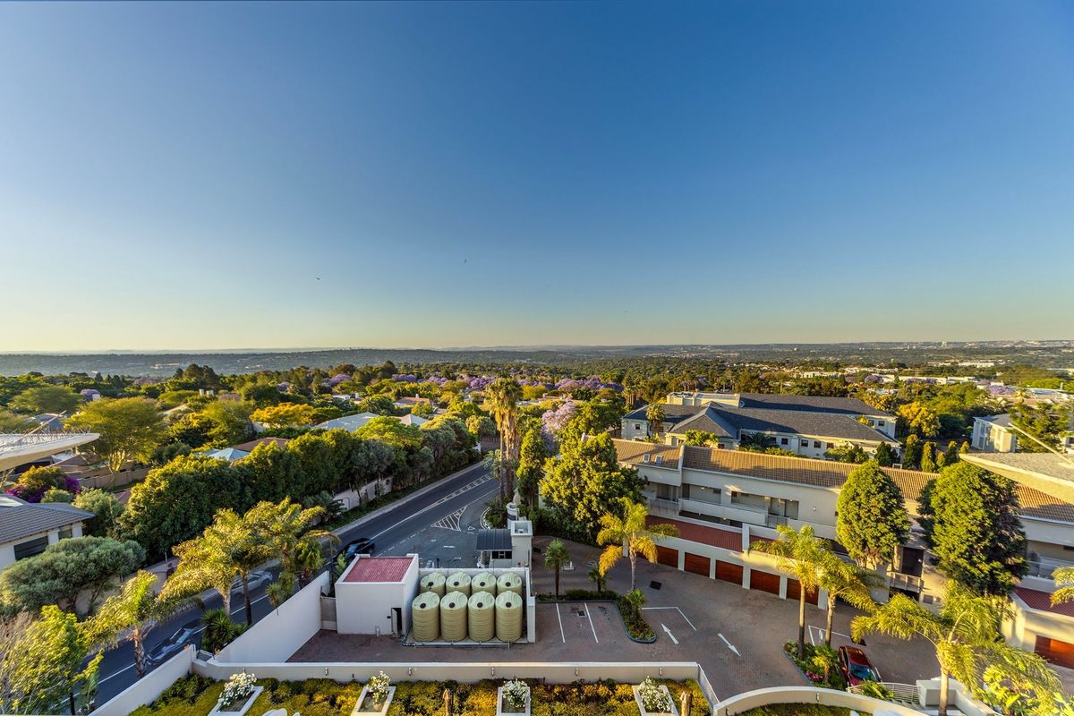 An elevated aerial view of the property grounds, featuring a security gatehouse, water storage tanks, paved driveway, and surrounding landscaped residential area.