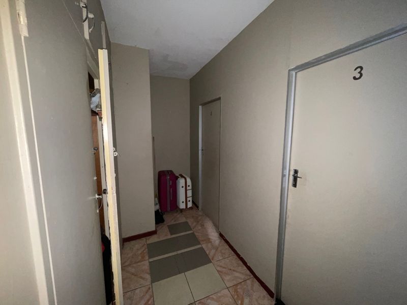 A functional apartment hallway featuring tiled flooring and multiple internal access doors, showing signs of ceiling water damage.