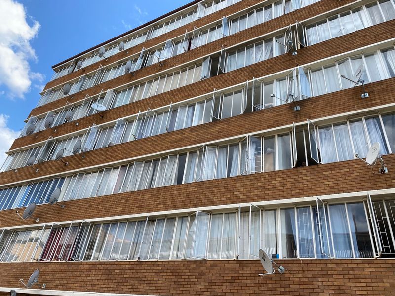 Exterior view of a multi-story apartment building featuring a classic brick facade and numerous casement windows with mounted satellite dishes.