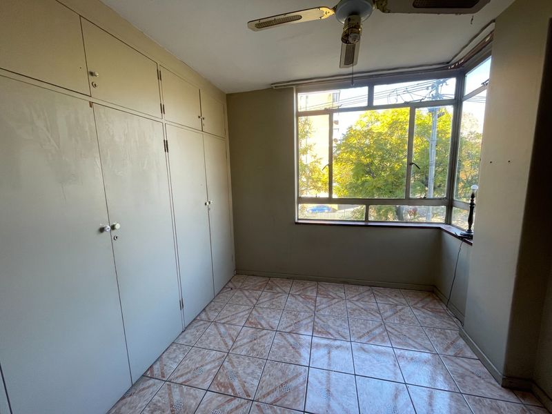 An empty bedroom featuring built-in cupboards, tiled flooring, and a ceiling fan, offering a blank canvas for renovation and modernization.