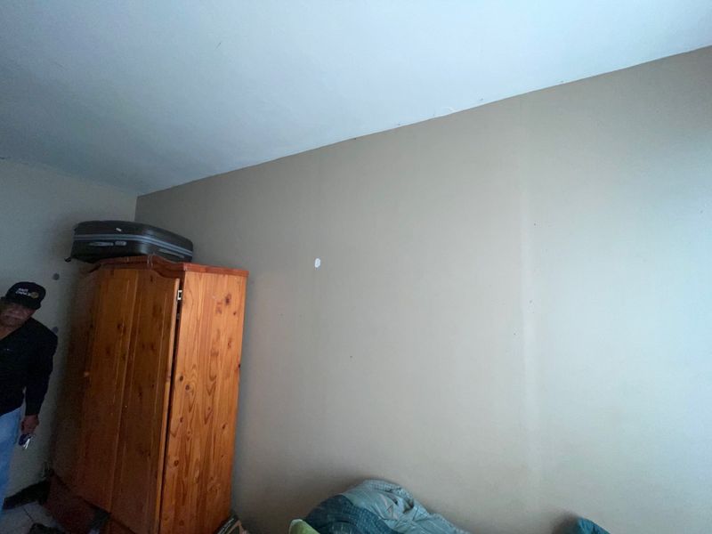 A bedroom interior featuring plain painted walls with visible surface wear and minor imperfections.