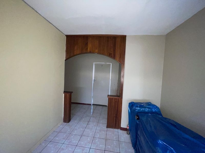 An empty living area featuring tiled flooring and a decorative wooden archway leading to an internal doorway.