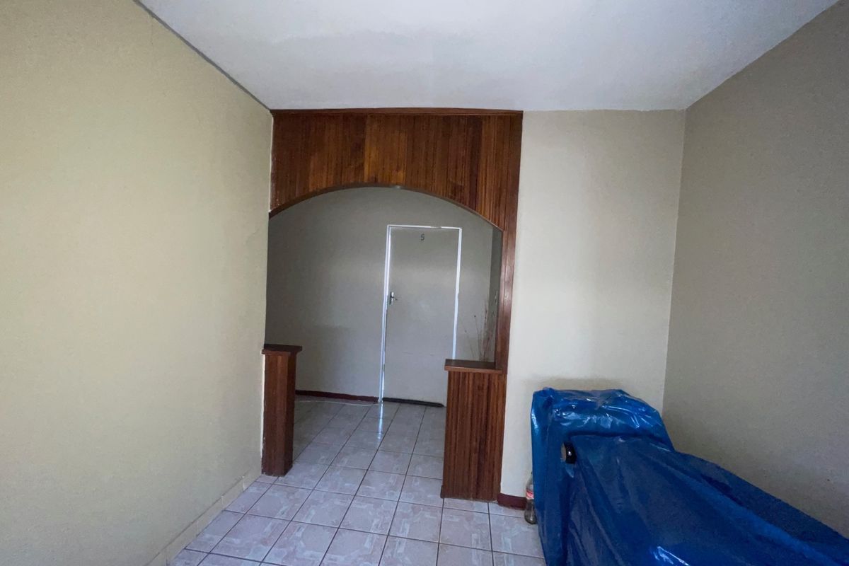 An empty living area featuring tiled flooring and a decorative wooden archway leading to an internal doorway.