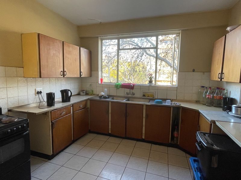 A dated kitchen featuring original wooden cabinetry, tiled backsplash, and tiled flooring, offering a functional layout with potential for modern renovation.