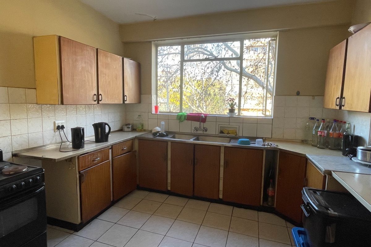 A dated kitchen featuring original wooden cabinetry, tiled backsplash, and tiled flooring, offering a functional layout with potential for modern renovation.