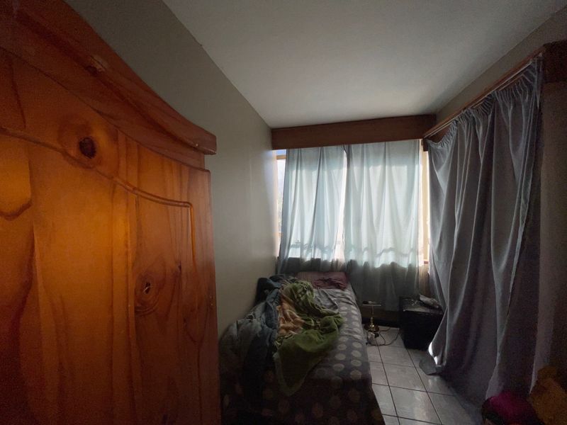 A compact bedroom featuring tiled flooring and window curtain tracks, offering a functional space for a single bed.