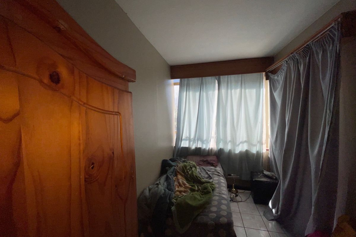 A compact bedroom featuring tiled flooring and window curtain tracks, offering a functional space for a single bed.