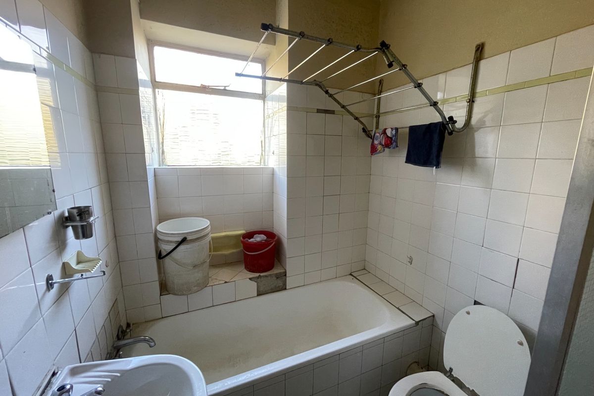 A dated bathroom featuring a bathtub, pedestal basin, and toilet, with visible wear to the wall tiles and grout requiring renovation.