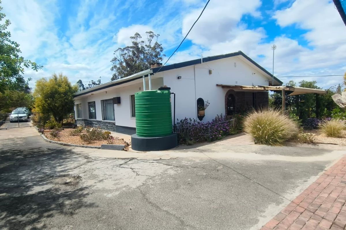 Rear exterior view of the house featuring a paved driveway, water storage tank, and established garden area.