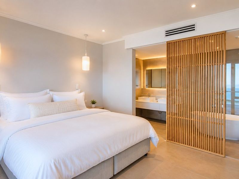Modern bedroom featuring an open-plan ensuite with a freestanding bathtub, glass shower, double vanity, and a stylish timber slat privacy screen.
