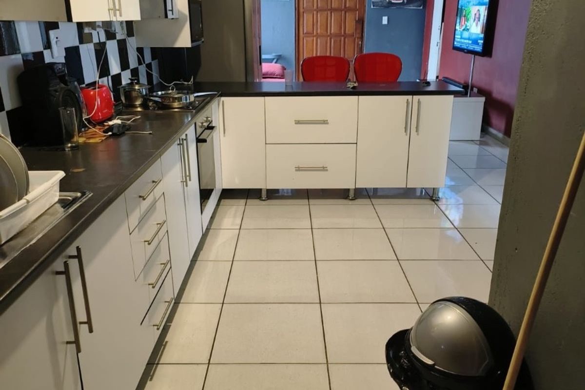 Open-plan kitchen featuring white cabinetry, dark countertops, and tiled flooring, seamlessly flowing into the adjacent living area.